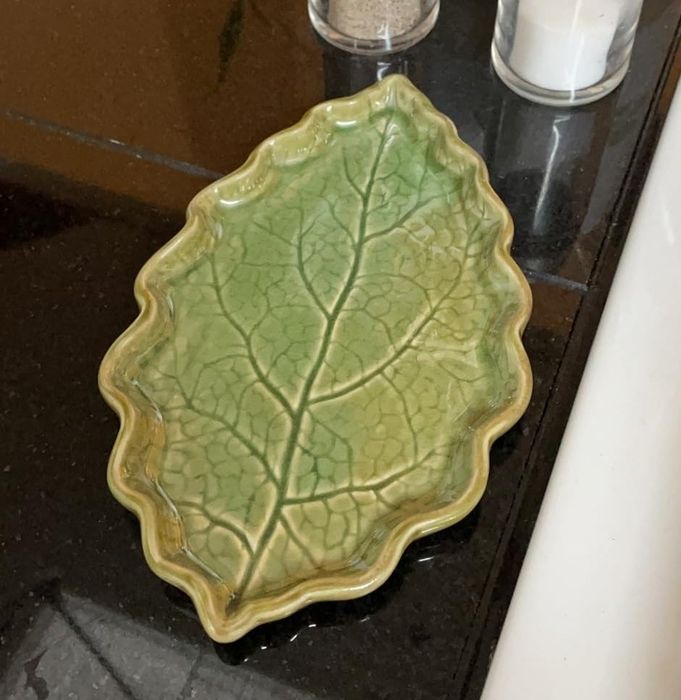 A green, leaf-shaped dish placed next to salt and pepper shakers on a kitchen counter.