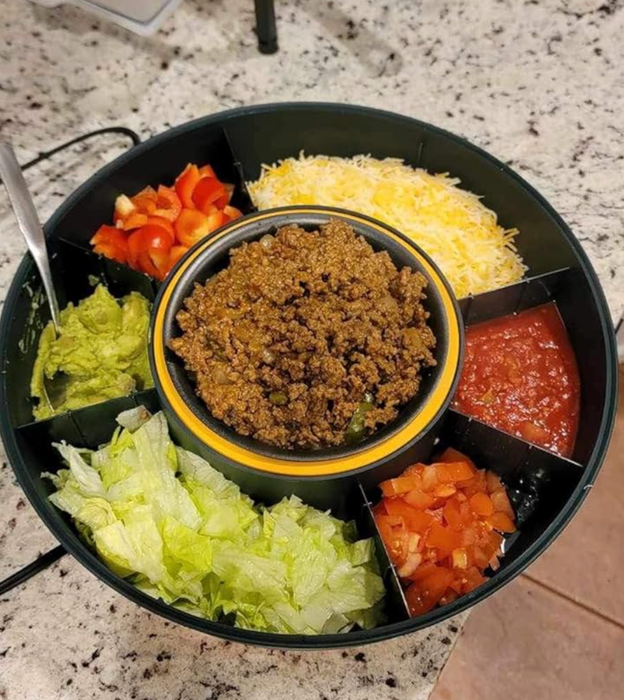 A round tray with sections filled with taco ingredients: ground meat, lettuce, cheese, tomatoes, salsa, and peppers