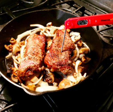 Reviewer photo of a meat thermometer inserted into a steak sizzling in a skillet on the stove.