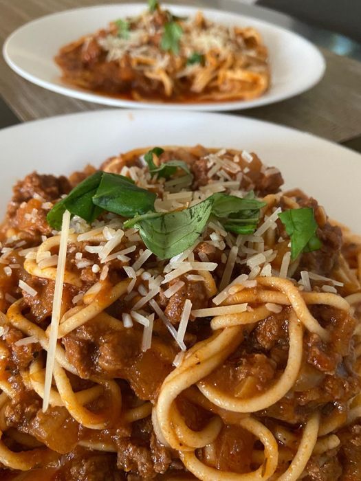 A review photo of two plates of homemade spaghetti topped with a rich tomato meat sauce