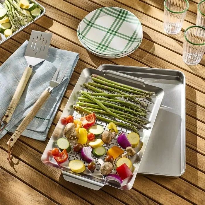 Grill pan filled with a colorful mix of grilled vegetables like asparagus, tomatoes, and mushrooms, placed on a checkered tablecloth with grilling tools nearby on a wooden surface