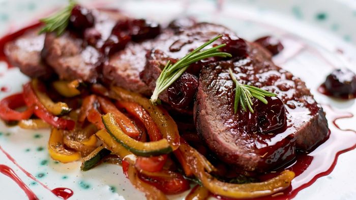 Five slices of roast beef topped with a roasted cherry sauce rest on a bed of roasted pepper slices.
