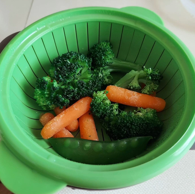 A steamer filled with broccoli, carrots, and snow peas ready to cook.