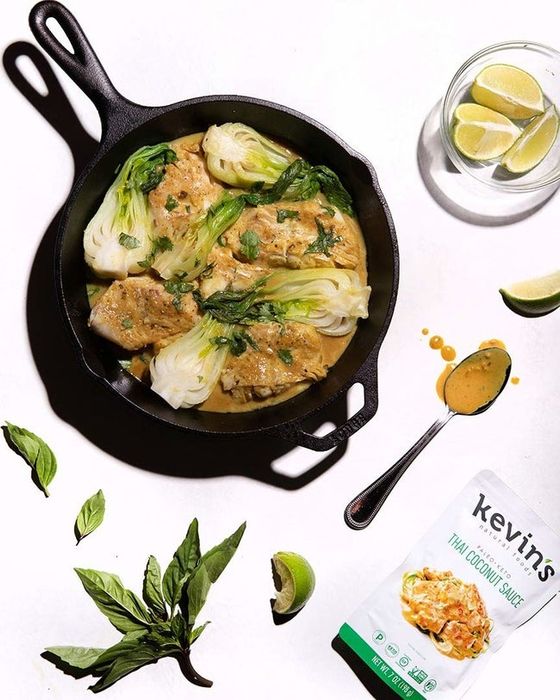 A cast-iron pan sizzling with Thai Coconut Sauce, chicken, and bok choy cooking together.