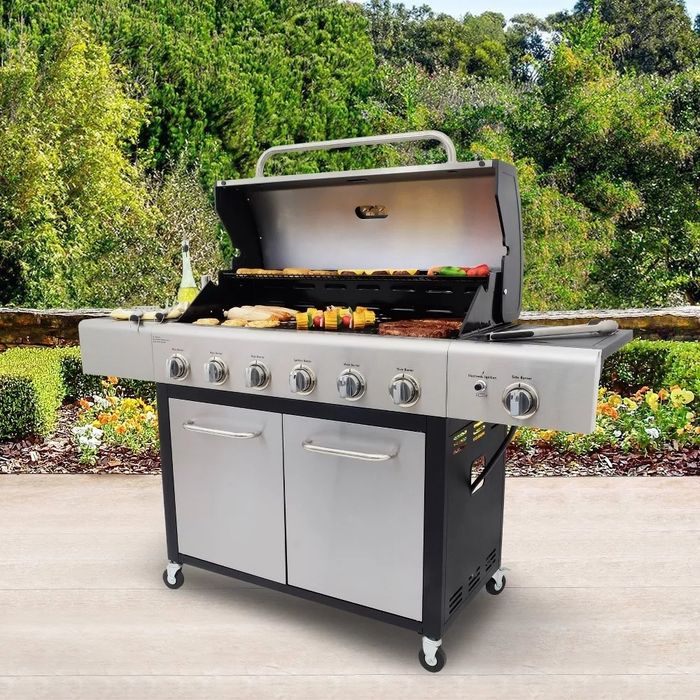 A spacious outdoor stainless steel gas grill with multiple burners and storage options, set against a beautiful garden with neatly trimmed bushes and lush greenery in the background.