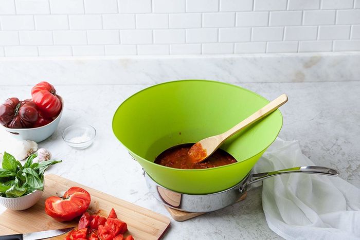 A large green mixing bowl filled with tomato sauce, accompanied by a wooden spoon. Fresh tomatoes, basil, and garlic cloves neatly arranged on a cutting board beside it.