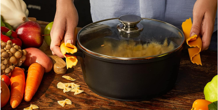 A person holding a pot lid with novelty pot handle rests, surrounded by fresh vegetables.