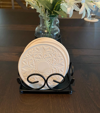 A set of lace-patterned white stone coasters arranged in a black holder
