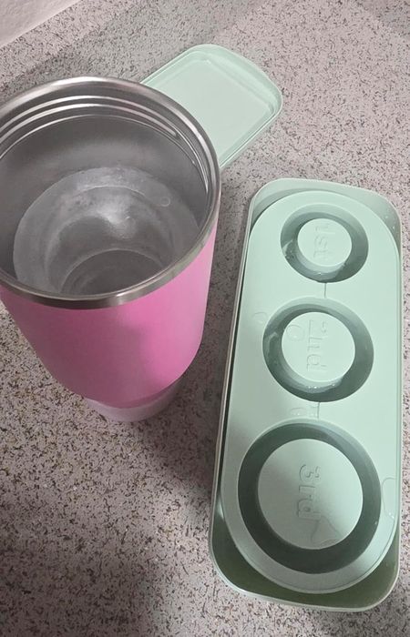 A pink tumbler alongside a green ice cube tray with labeled sections