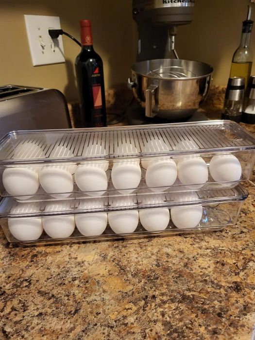 Two transparent egg containers filled with white eggs sit on a kitchen counter, surrounded by a toaster, wine bottles, and a mixer