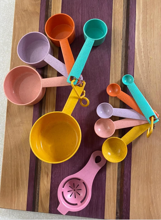A set of bright, colorful measuring cups placed alongside a citrus juicer on a wooden board