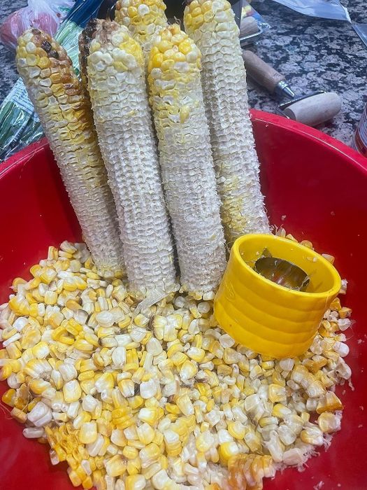 Corn cobs with kernels removed, displayed in a red bowl with loose kernels and a yellow corn stripper tool. Featured in a shopping guide
