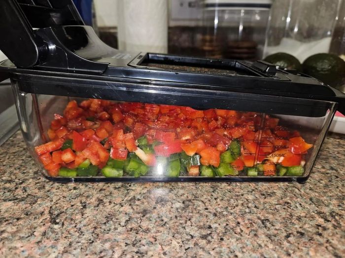 Chopped vegetables neatly arranged in a transparent food container with measurement markings, placed on a kitchen counter.