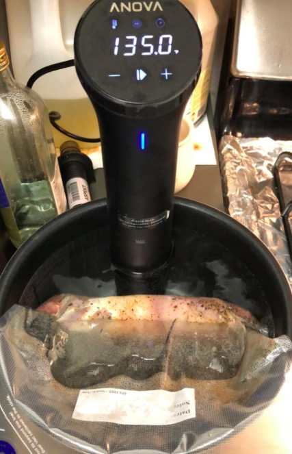 The sous vide cooker in action, placed in a pot with a piece of meat cooking inside