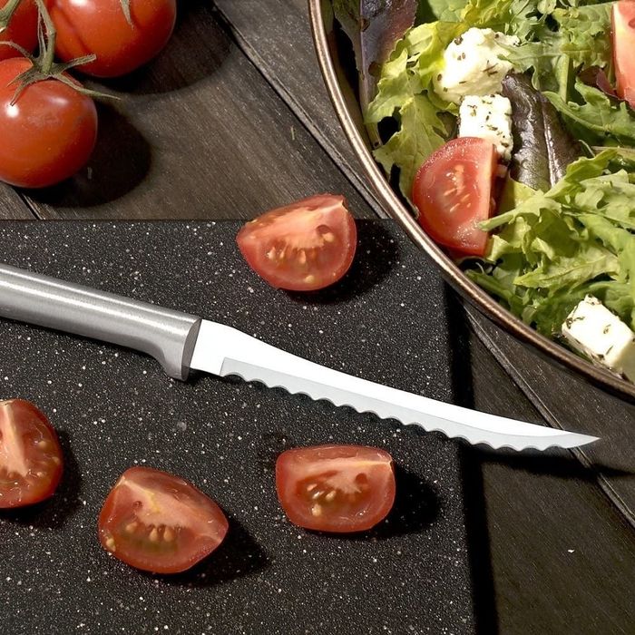 A serrated knife resting next to freshly chopped cherry tomatoes.
