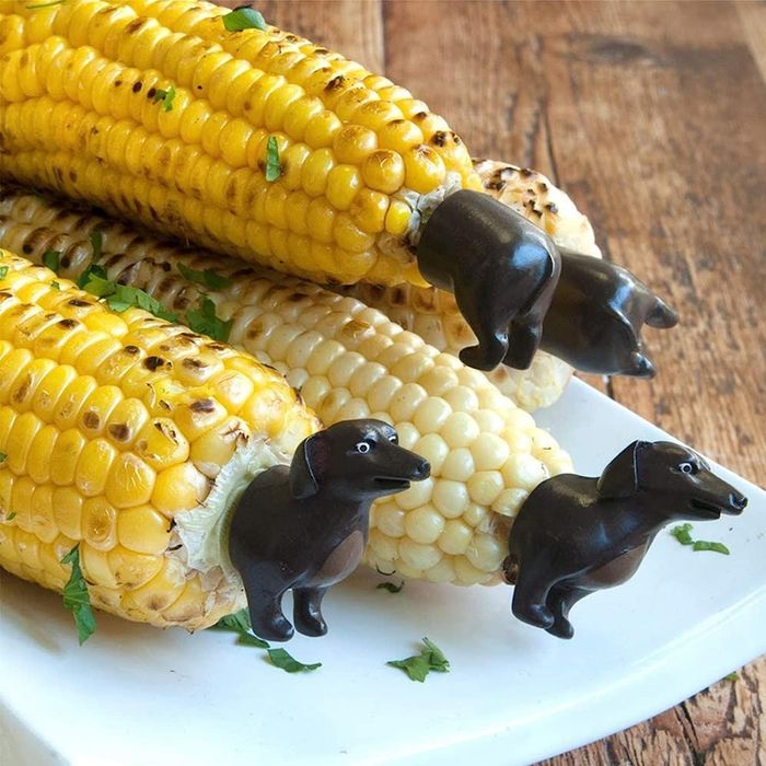 Corn cobs with unique corn holders shaped like dog faces and rear ends placed on either side of the corn.