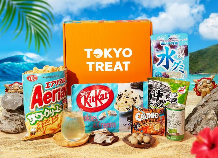 Tokyo Treat snack box showcasing various Japanese treats, such as KitKat, Aerial chips, Crunky chocolate, and UHA gummies, arranged on a picturesque beach setting.
