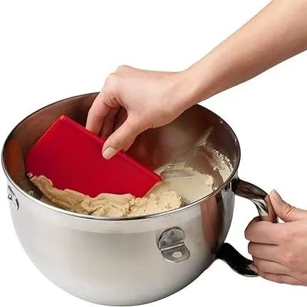A person using a red spatula to mix ingredients in a bowl—an essential tool for home baking