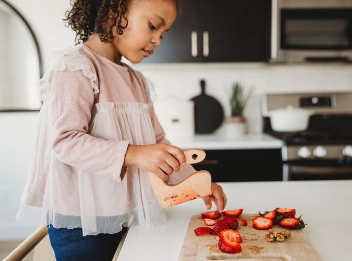 A child slicing strawberries with the wooden knife.