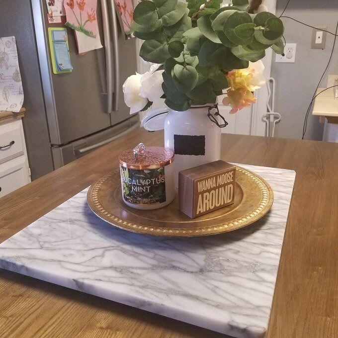 A collection of scented candles on a marble tray resting on a wooden table, paired with a vase of flowers, creating a cozy home ambiance