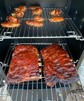 A close-up view of two racks of ribs and wings slowly cooking inside the reviewer’s smoker.