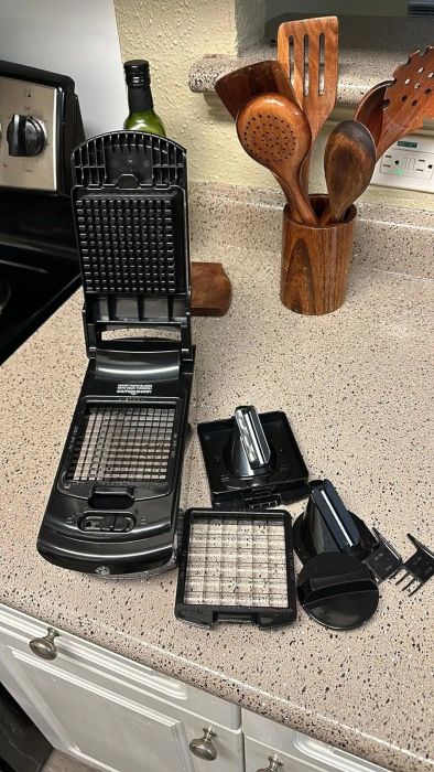 A vegetable chopper sits on a kitchen counter with its various interchangeable plates neatly laid out beside it.