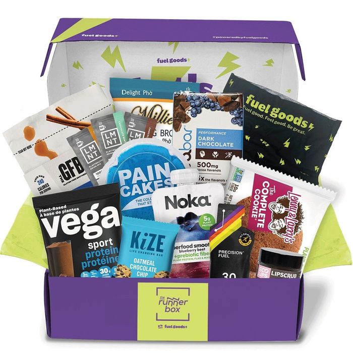A box filled with various snacks and nutritional items perfect for fitness lovers. Brands like Vega, Noka, and Fuel Goods are included.
