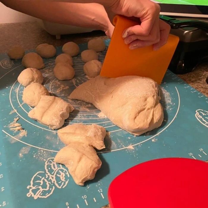 A person slicing dough into sections on a kitchen counter in preparation for baking