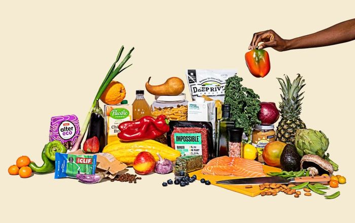 A table filled with a selection of fresh groceries and packaged foods, showcasing fruits, vegetables, salmon, and plant-based options.