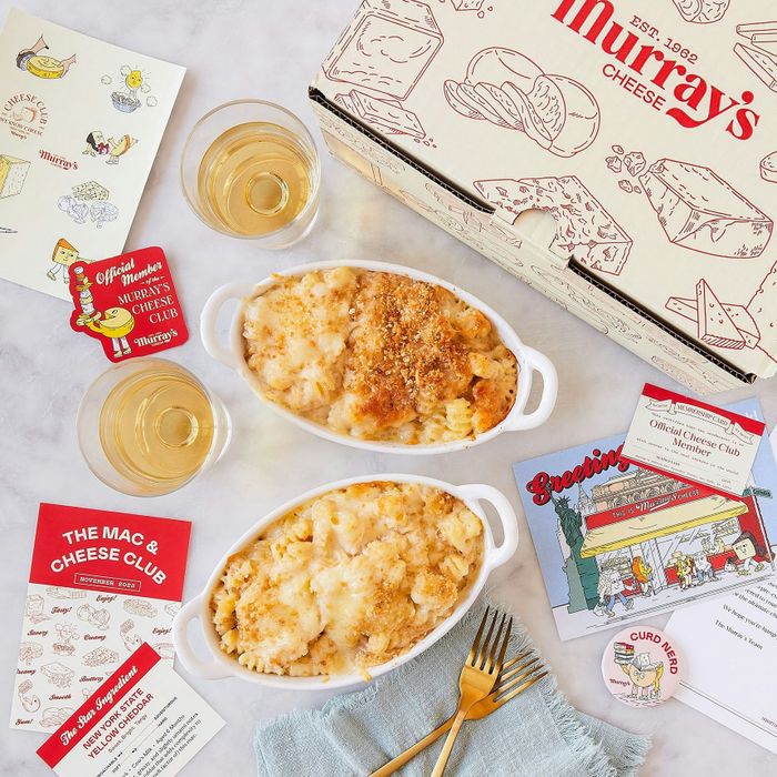 Two servings of macaroni and cheese, topped with golden breadcrumbs, placed next to a Murray's Cheese box along with various promotional materials.