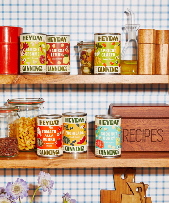 Six cans of uniquely flavored beans neatly arranged on a pantry shelf.