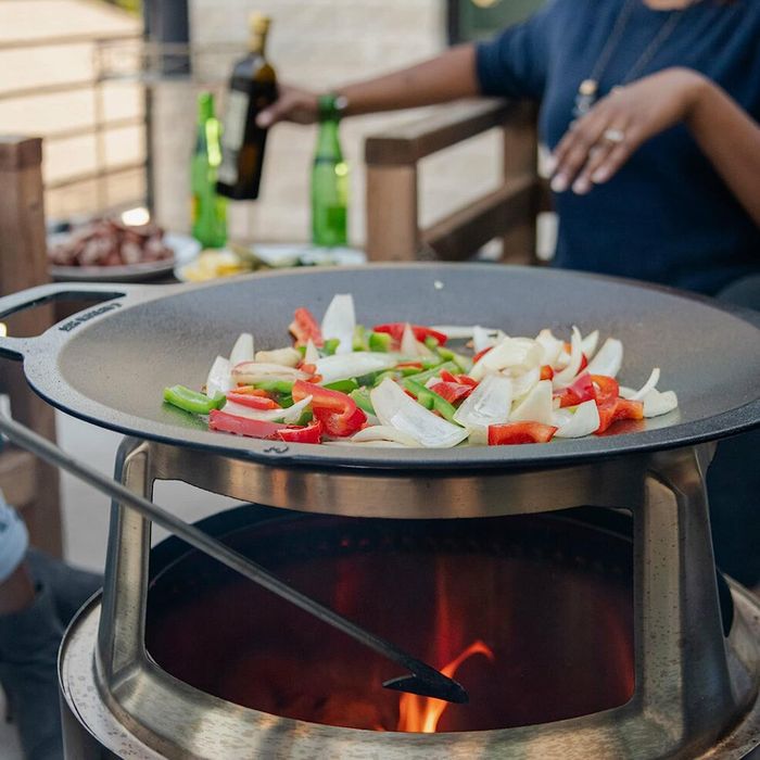 A wok top positioned on a stand above a Solo Stove, while two people prepare food.
