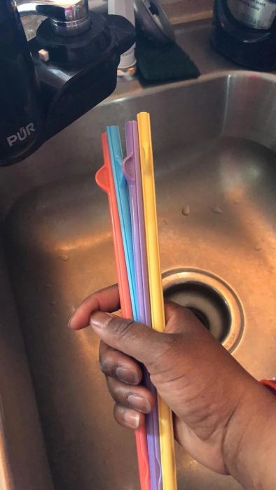 A hand holding several colorful silicone straws over a sink, demonstrating a reusable option for eco-friendly shoppers