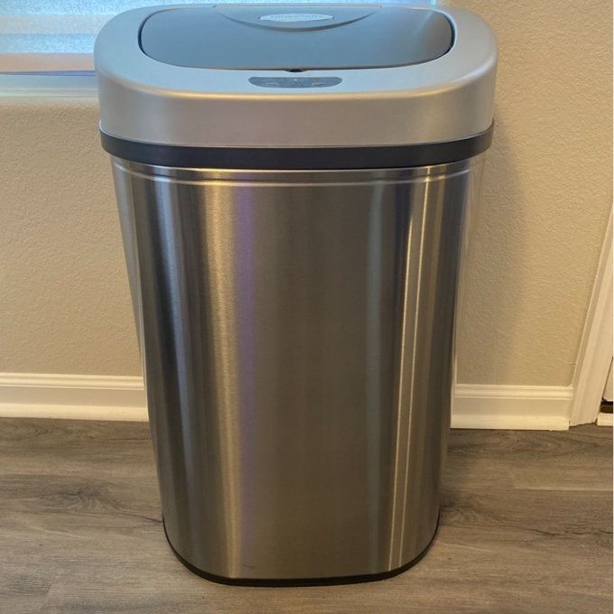 A stainless steel, sensor-operated trash can in a home environment, with a lid that opens automatically