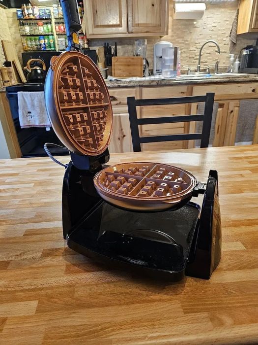 A freshly cooked waffle placed on a kitchen counter with the waffle maker open beside it, showcasing the perfectly made treat.