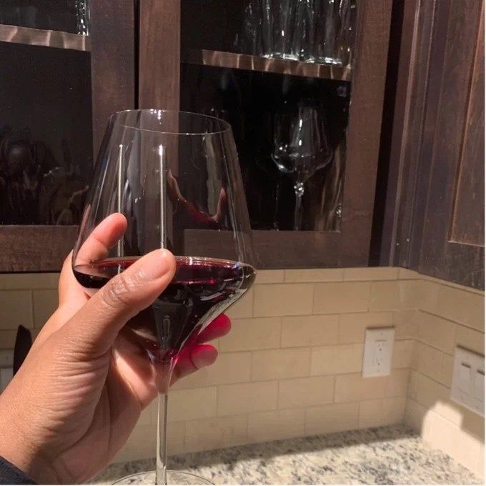 A reviewer holding a wine glass filled with rich red wine.