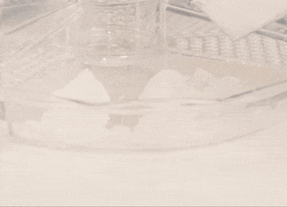 A bowl being filled with crystal-clear gel and ice cubes, carefully placed with a pair of tongs