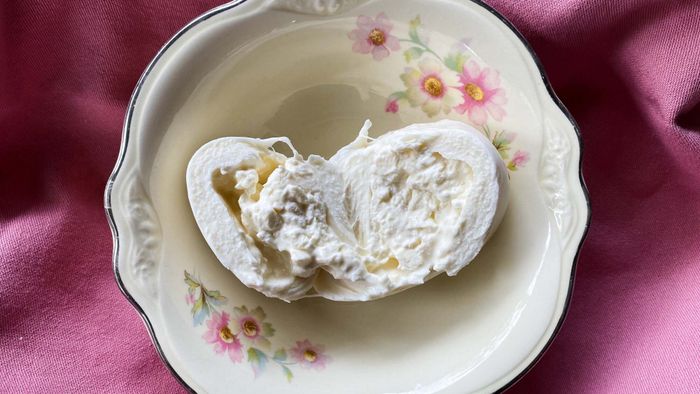 A cross-section of burrata cheese placed in a bowl, resting on a mauve napkin.