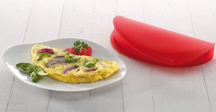 An omelet served on a plate next to the red silicone mold.