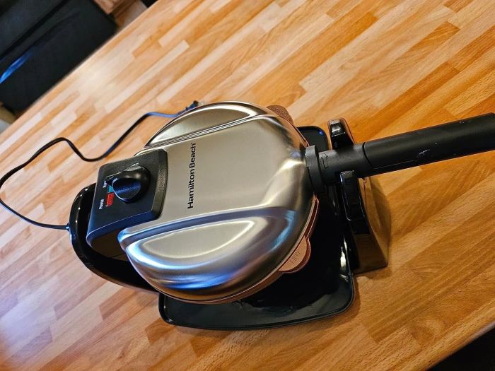 A sleek Hamilton Beach vacuum cleaner resting on a wooden floor, seen from above with the handle extended, ready to tackle the cleaning job.