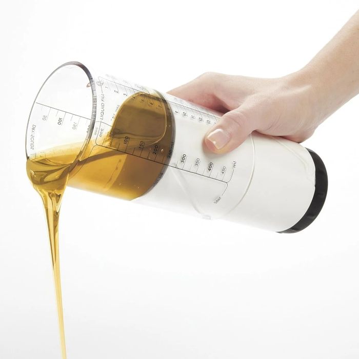A hand pouring honey from a transparent, measuring dispenser against a white background.