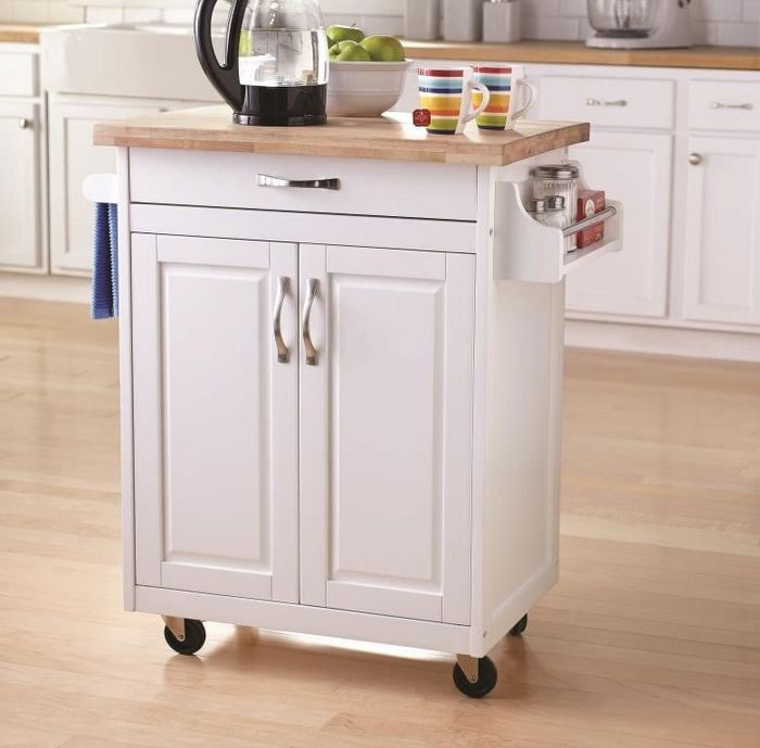 A white kitchen cart with a wooden top, featuring a drawer, lower cabinet, towel rack, and cup holders, placed in a modern kitchen with light hardwood flooring