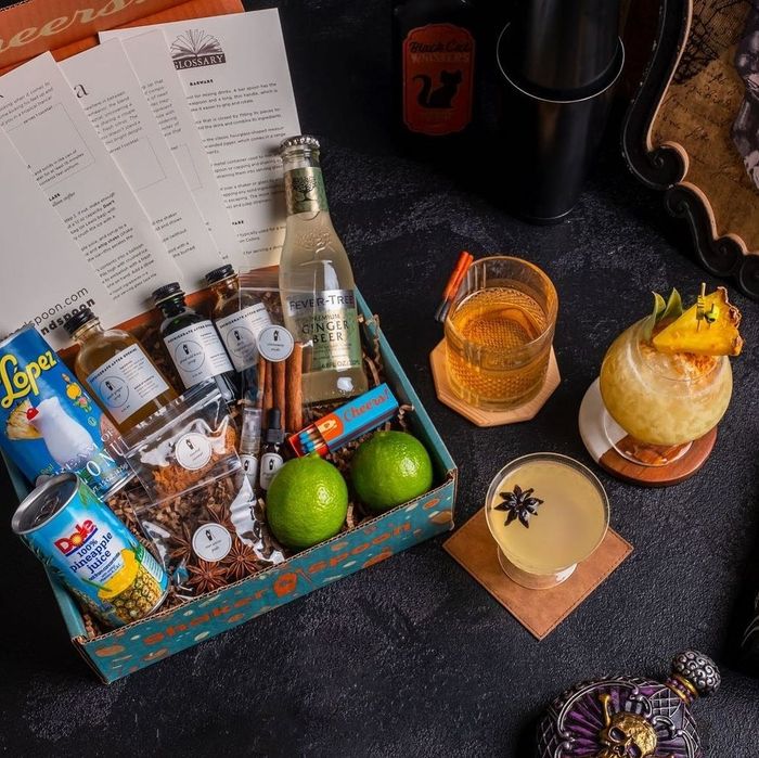 A top-down view of an open box filled with cocktail ingredients, next to three ready-made drinks.