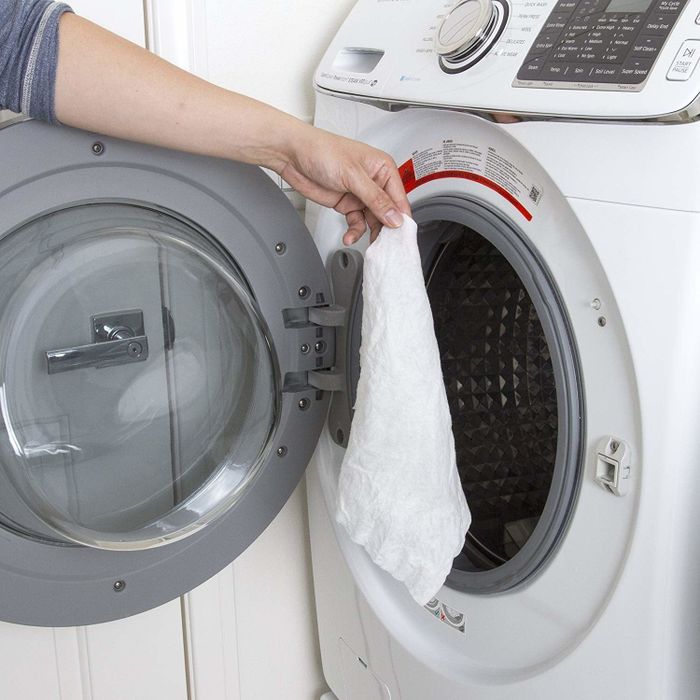 A hand placing the bamboo towel into a washing machine.
