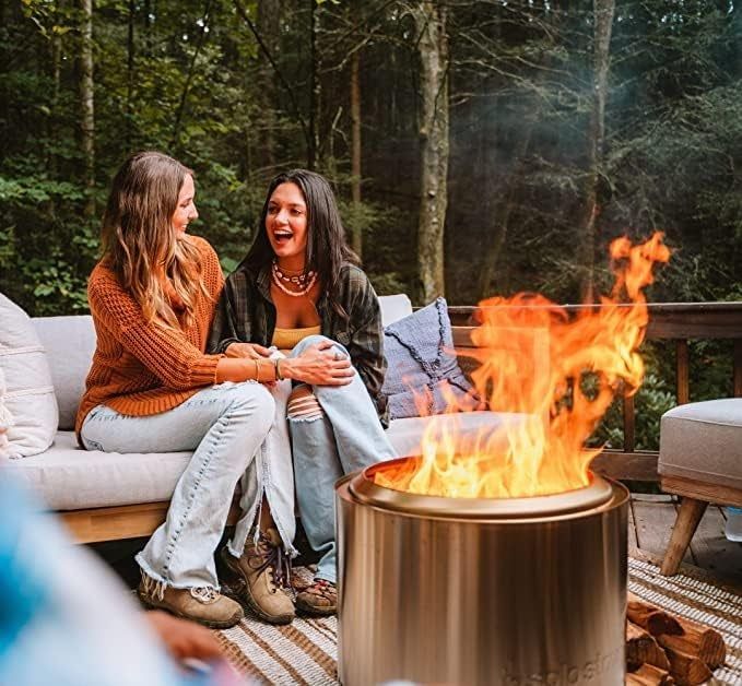 A couple lounging on an outdoor sofa with a cozy fire burning on their porch.
