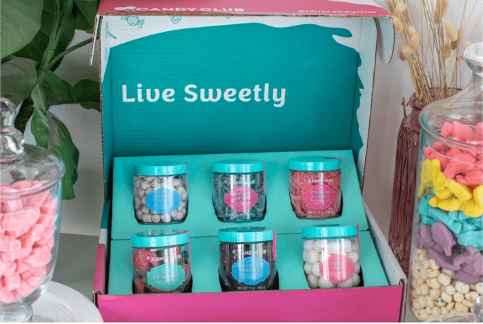 An open Candy Club box displaying six jars filled with assorted candies. The box features text reading, 