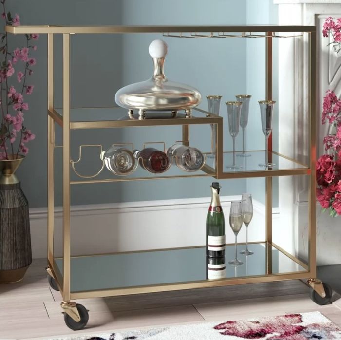 A gold-tone bar cart featuring a wine rack, glasses, and bottles neatly arranged on it