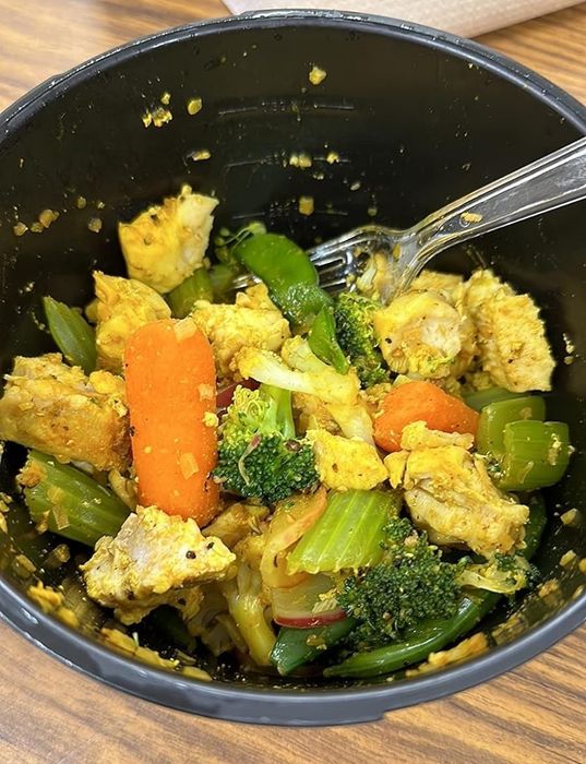 A bowl filled with cooked vegetables and chicken pieces, accompanied by a fork, resting on a wooden table—ideal for a nutritious meal