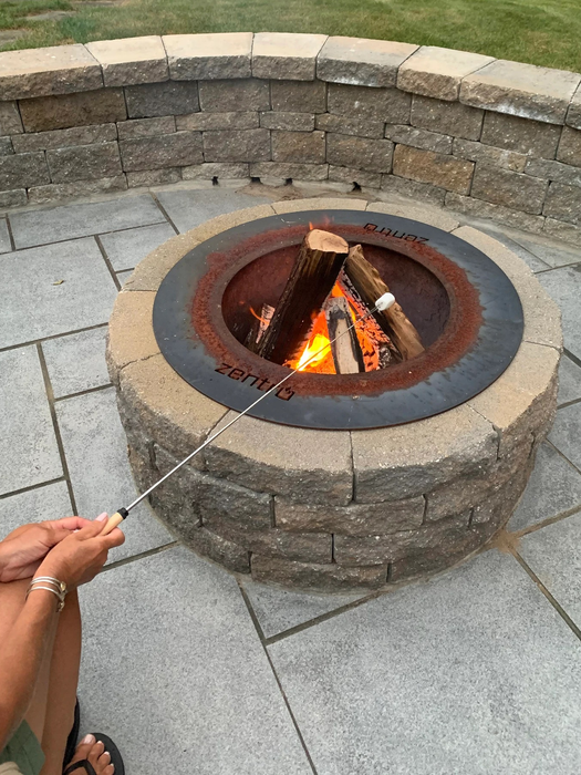 A person roasting a marshmallow over a fire pit, using a long roasting stick