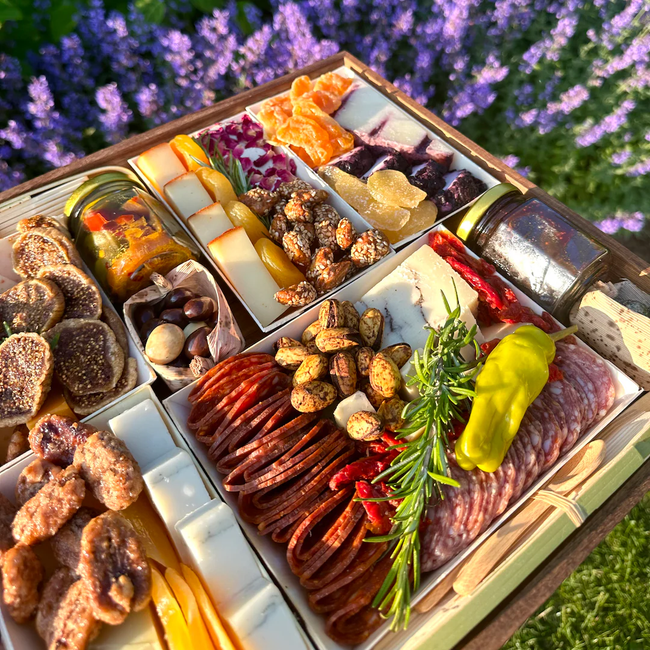 A deluxe charcuterie board featuring an assortment of meats, cheeses, nuts, and fruits, beautifully arranged outdoors